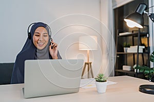 Asia muslim lady wear headphone watch webinar listen online course communicate by conference video call at night home office.