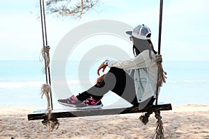 Asia woman sitting alone on wooden chair rope on beach looking t