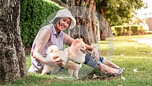 Asia women sitting on grass under a tree in the garden with lovely puppy pomeranian dog on travel tip