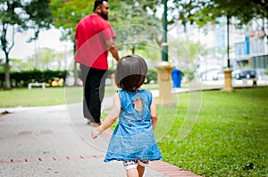 Asian 1 year old toddler is busy walking with her father in a tropical park in the morning. Exploration and fatherhood concept