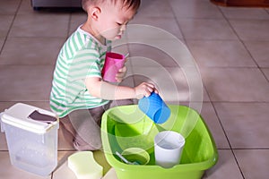 Asian 18 months old toddler boy child having fun pouring water into cup, Wet Pouring Montessori Preschool Practical Life Activitie