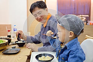 Asian 18 months toddler baby boy child eating food with fork & spoon by himself at Japanese restaurant, Dad proud of hime