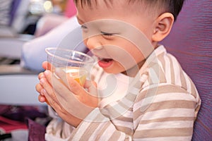 Asian 2 - 3 years old toddler baby boy child drinking orange juice during flight on airplane. Flying with children