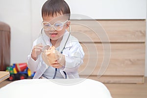 Asian 2 - 3 years old toddler boy child in doctor uniform playing doctor with plush toy at home