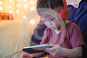 Asian 2 -3 years old toddler boy child listening to music with headphones from smartphone, Kids playing with phone in bedroom at h