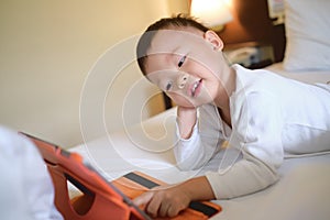 Asian 2-3 years old toddler boy child sitting in bed watching a video from tablet pc