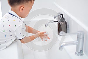 Asian 2 - 3 years old toddler boy child washing hands by himself on sink and water drop from faucet in public toilet / bathroom