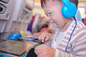 Asian 2 - 3 years old toddler boy child wearing headphones using tablet pc watching cartoons / playing game during flight on