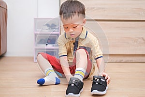 Asian 2 - 3 years old toddler boy sitting and concentrate on putting on his black shoes / sneakers