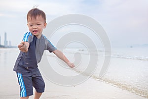 Asian 2 years old toddler baby boy child on beach with dirty hands covered with wet sand