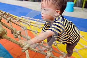 Asian 2 years old toddler baby boy child having fun trying to climb on jungle gym at indoor playground