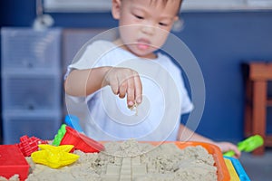Asian 2 years old toddler boy playing with kinetic sand in sandbox at home