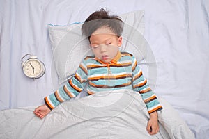Asian 3 - 4 years old toddler boy kid taking a nap, sleeping on his back with alarm clock, The importance of sleep in child