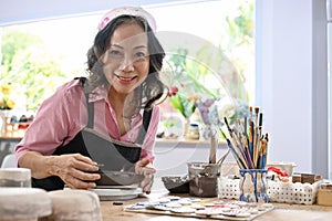 Asian 60s aged woman making a clay ceramic plate on worktable in the studio