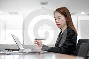Asian accountant business woman working on desk and looking at laptop in office interior background