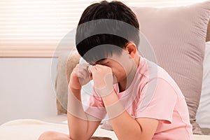 Asian adorable boy crying on bed because he didn`t go out to play with his friends on holiday. young children making mistakenly