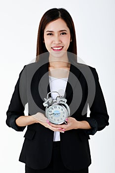 Asian adorable business woman with long hair wearing formal black suit, smiling, looking and holding alarm clock with isolated