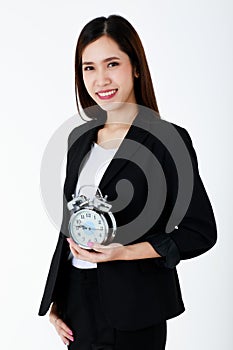 Asian adorable business woman with long hair wearing formal black suit, smiling, looking and holding alarm clock with isolated