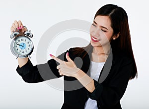 Asian adorable business woman with long hair wearing formal black suit, smiling, looking and pointing at alarm clock with isolated