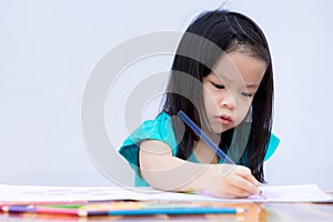 Asian adorable girl is doing homework. Children paint with wooden colors on a coloring book. White paper. Child learn art.