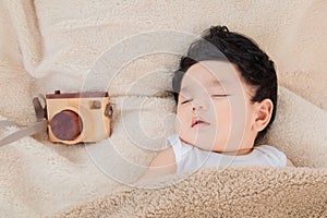 Asian adorable newborn baby deeply sleeping and napping with beige blanket next to toy camera with safe and comfortable. Sweet