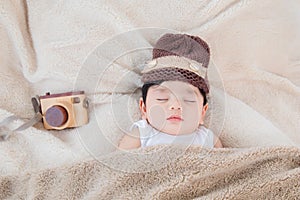 Asian adorable newborn baby deeply sleeping and napping with beige blanket next to toy camera with safe and comfortable. Sweet