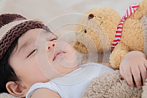 Asian adorable newborn baby wear brown knit hat deeply sleeping with beige blanket next to teddy bear and toy camera with safe and