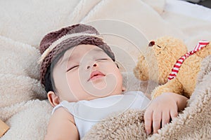 Asian adorable newborn baby wear brown knit hat deeply sleeping with beige blanket next to teddy bear and toy camera with safe and