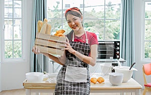Asian adorable pretty beautiful woman smiling with happiness, holding and showing wooden basket of baked bread while staying at