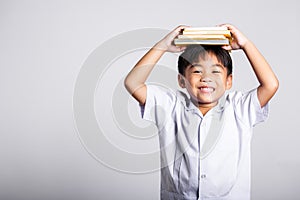 Asian adorable toddler smiling happy wear student thai uniform red pants stand holding book over head and screaming