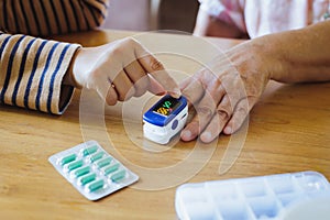 Asian adult daughter assistance her senior mother measuring for blood oxygen levels on finger with pulse oximeter monitor