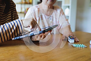 Asian adult daughter assistance her senior mother measuring for blood oxygen levels on finger with pulse oximeter monitor