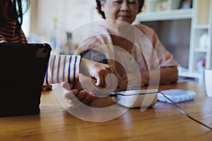 Asian adult daughter assistance her senior mother measuring blood pressure and heart rate with digital pressure gauge electric