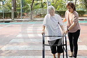 Asian adult daughter assistance and support her senior mother to cross the street,elderly woman with walker on the crosswalk,