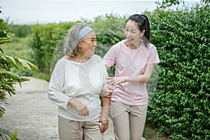 asian adult daughter hug her senior mother in backyard garden at home . young woman embrace old mom to take care in park