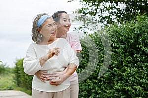 asian adult daughter hug her senior mother in backyard garden at home . young woman embrace old mom to take care in park