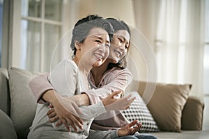 Asian adult daughter and senior mother hugging each other at home