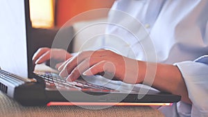 Asian adult hands using laptop computer with pillow support under, typing on notebook keyboard while sitting on sofa, side view,