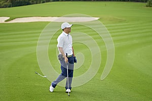 Asian golfer standing and watch after putting on green in golf course