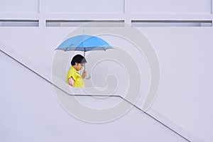 Asian adult plus size woman holding blue umbrella while walking down the stairs outside of white building