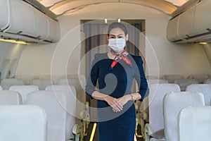 Asian air hostess in uniform standing in plane with wearing face mask