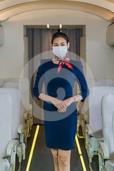 Asian air hostess in uniform standing in plane with wearing face mask
