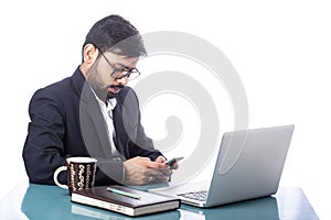 Asian ambitious business person typing on mobile phone distracted from working on laptop on desk