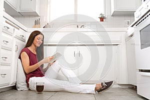 Asian american woman sitting on clean kitchen floor of her tiny home, enjoying leisure time with a book