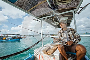 Asian angler holding fishing rod on a small fishing boat