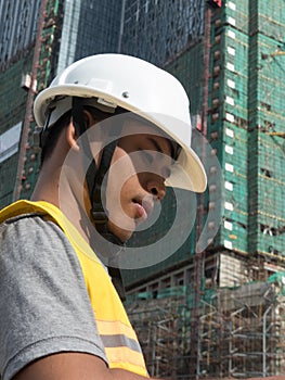 Asian architect profile looks down at plans with large housing project under construction in background