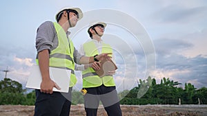 Asian architecture and engineer workers wear safety vest, safety helmet standing outside construction working field, teamwork