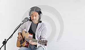 Asian artist singing song and playing acoustic guitar on white background for live acoustic concert and music related concept with