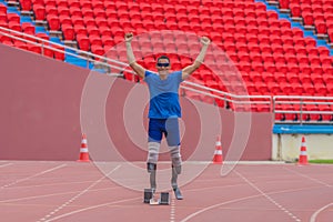 Asian athlete raises fists in confidence, ready at the start point on the stadium track with prosthetic running blades