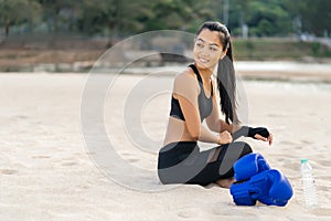 Asian athletic woman a fighter sitting on the beach before boxing training. Healthy lifestyle and summer mood.